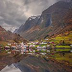Small homes on the shore of a fjord photographed from a Fjords sightseeing cruise boat leaving Flam in autumn, Norway