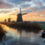 Three windmills, two rowboats and a canal in a rural landscape in Leidschendam, the Netherlands at sunrise in winter.